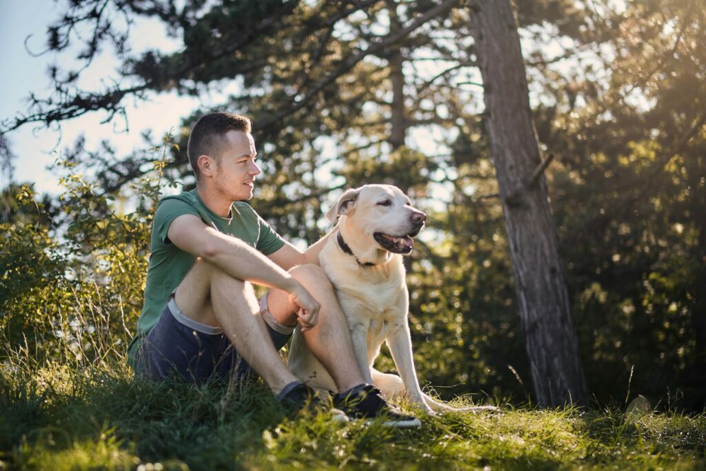 Mann sitzt mit seinem Hund im Wald und streichelt ihn